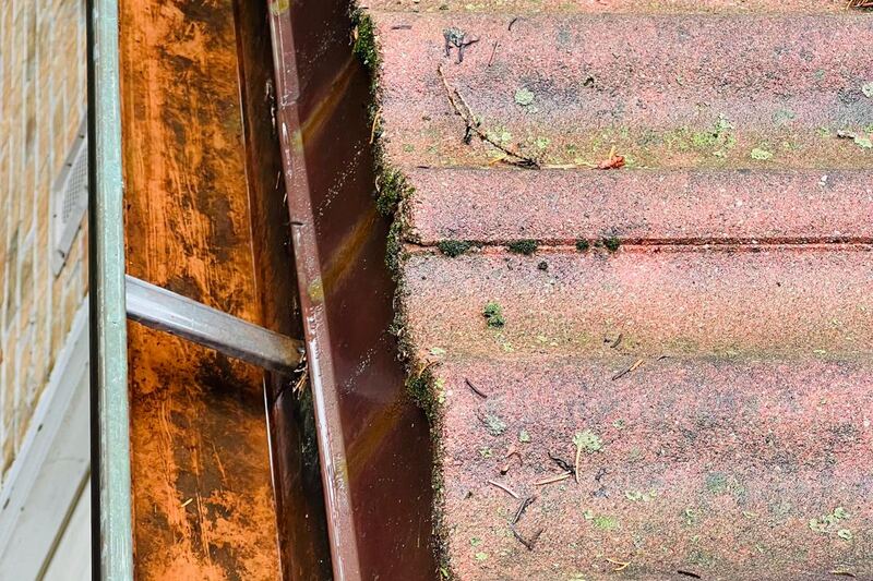 Copper-toned eavestrough running beside a moss-covered roof edge