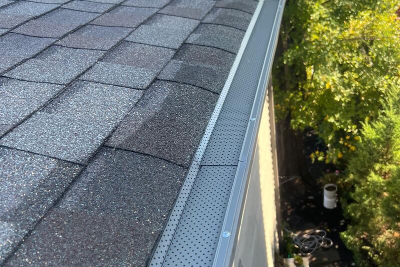 Perforated gutter guard along the edge of a shingled low-rise roof